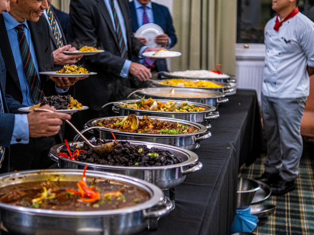 Guests in suits serving themselves from a buffet line at a corporate event, with a chef on hand